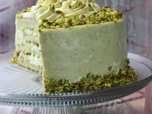 Vertical format photograph showcasing a single tall slice of the rich pistachio cake.