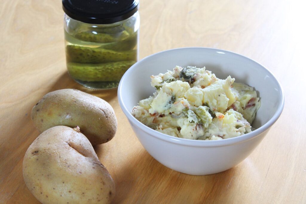Side perspective showing a bowl filled with creamy potato salad with pickle.