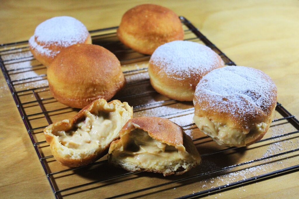 Presentation of the complete batch of freshly fried and dusted pastry cream filled berliners.
