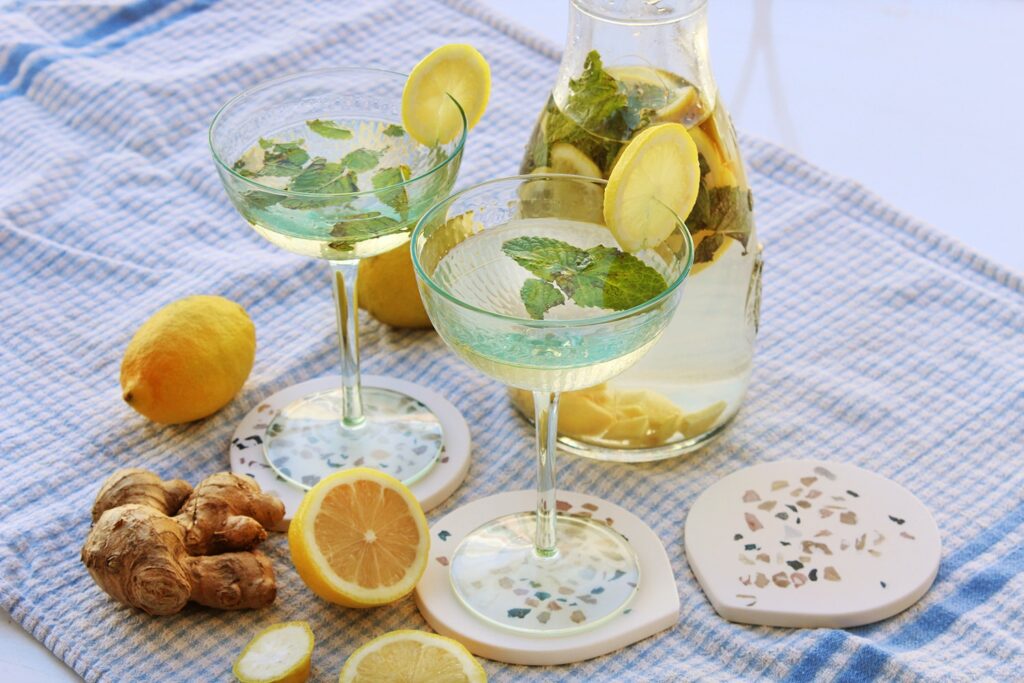 Side perspective displaying a tall refreshing glass pitcher filled with clear lemon ginger and peppermint water.