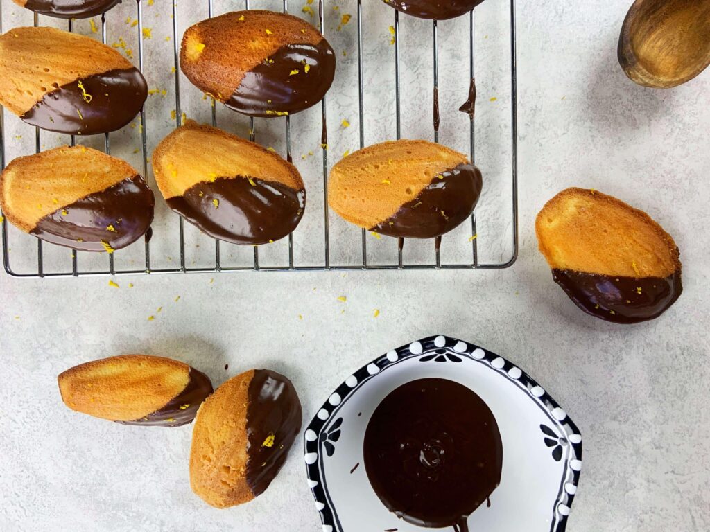 Presentation of a full scaled batch of beautiful shell-shaped orange madeleines with chocolate.