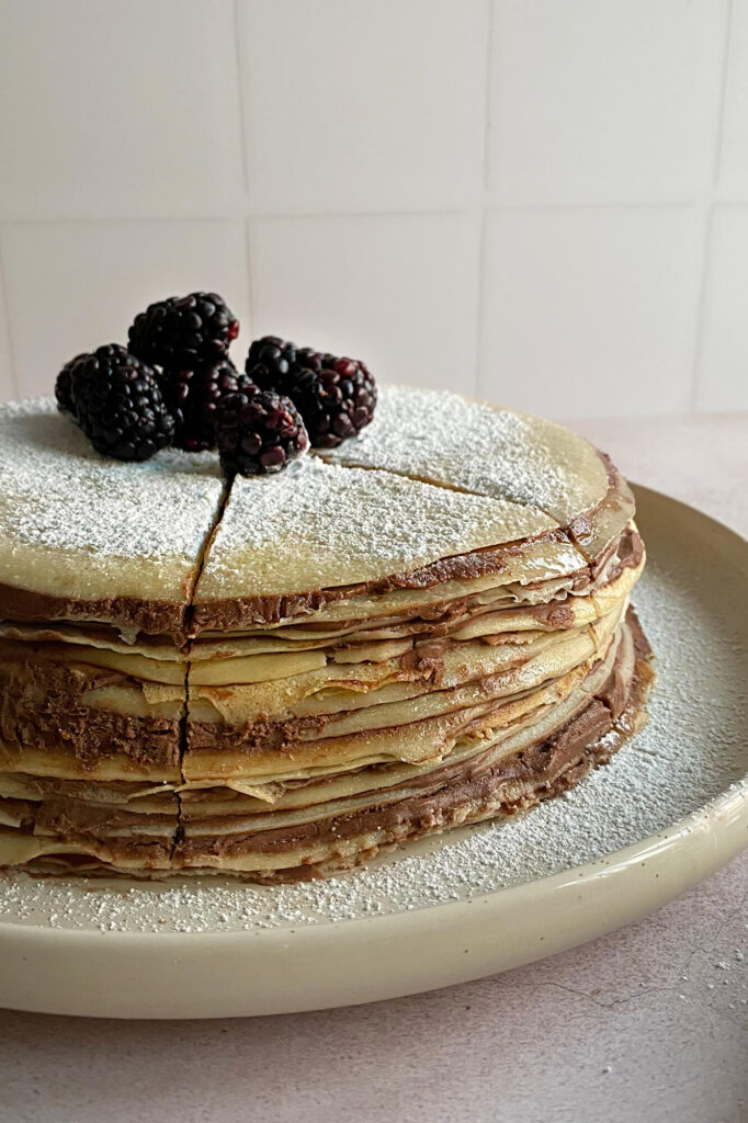 Fotografía en formato vertical centrada en la porción de pastel de crepas con nutella para servir.